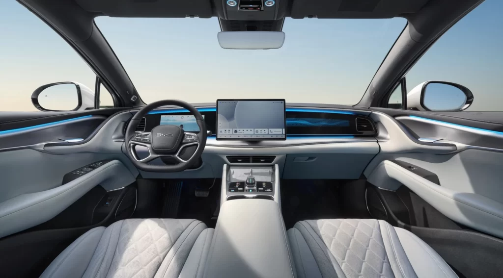 Interiøret i Sealion 7 4x4 sett fra baksetet, med digitalt dashbord, stor sentralskjerm og blå ambientbelysning.
