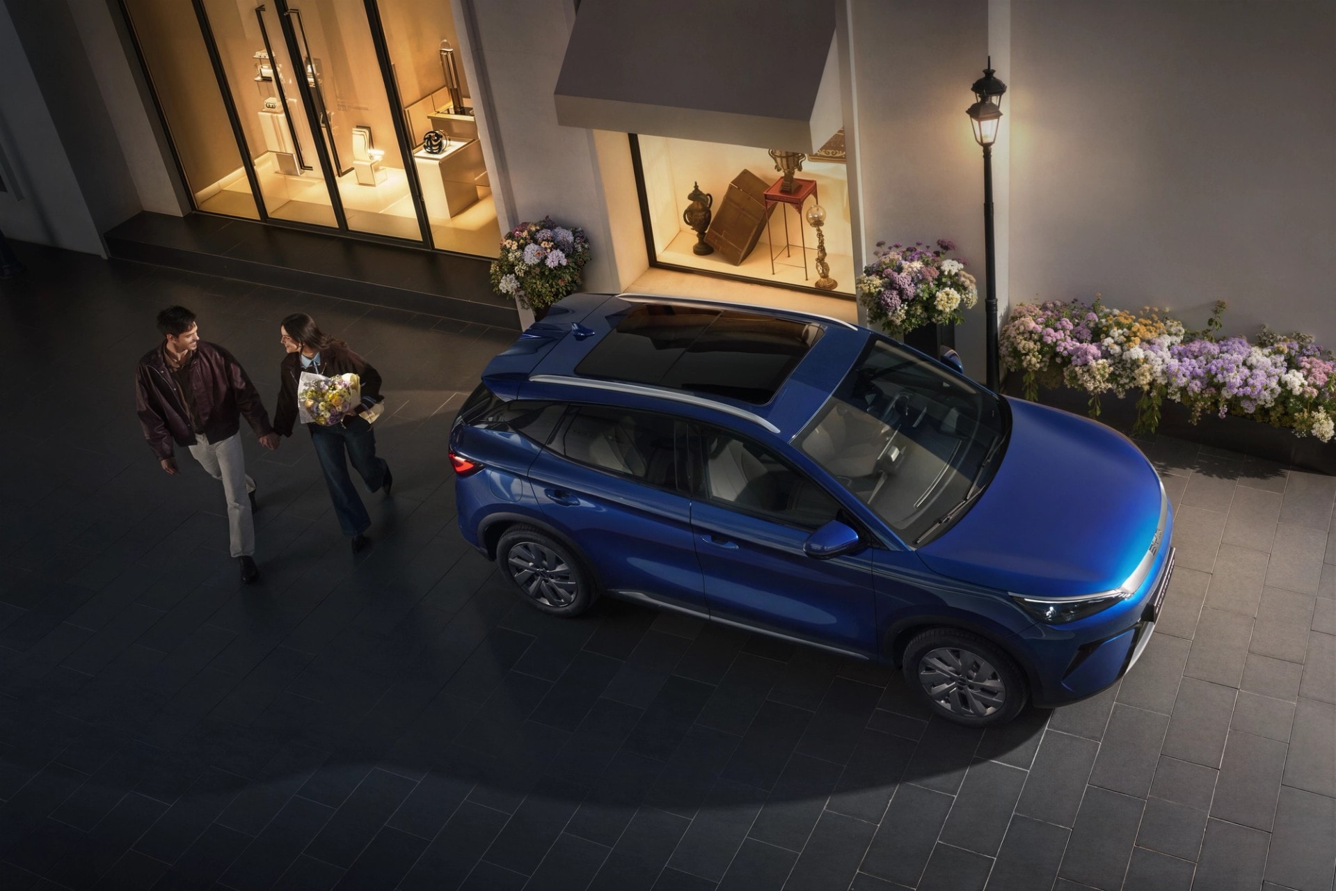 BYD EVO 4x4 parkert ved butikkfasade i kveldslys mens et par går forbi med blomster.